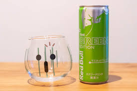 A product display image of the Red Bull Green Edition can alongside a glass filled with the poured energy drink, set against a white background to showcase its tropical color and presentation.