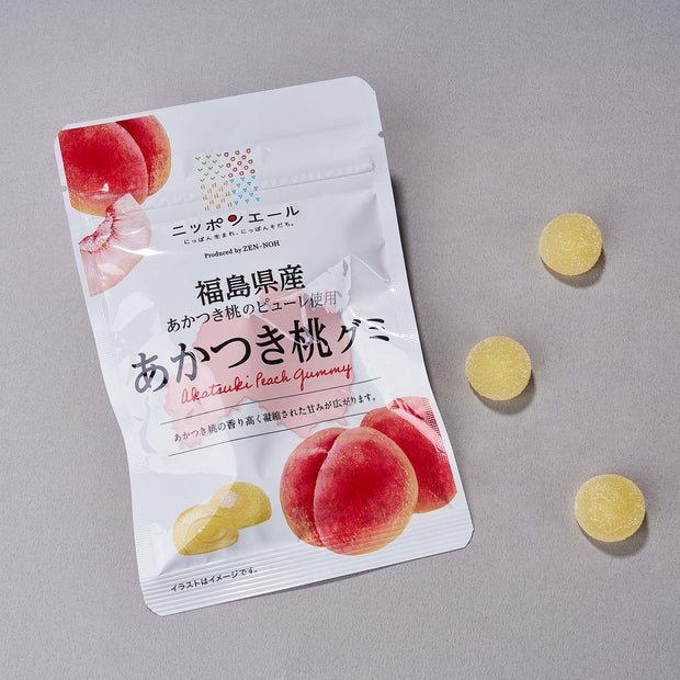 Three yellow peach-flavored gummies displayed on a plain white background, with the Zennoh Foods gummy pouch visible behind them.