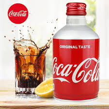 Image of the Coca Cola Original 300ml bottle can placed beside a glass filled with the beverage, showing its fizzy, dark cola appearance on a clean white background.
