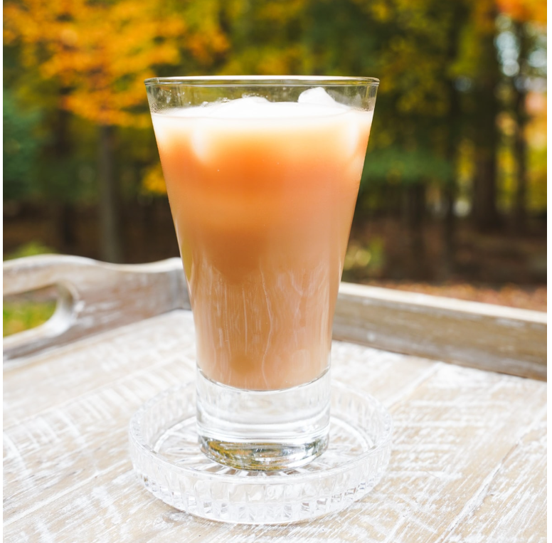 Coca Cola Kochakaden Royal Milk Tea poured into a glass, highlighting its smooth, creamy color and texture, with the bottle placed nearby.