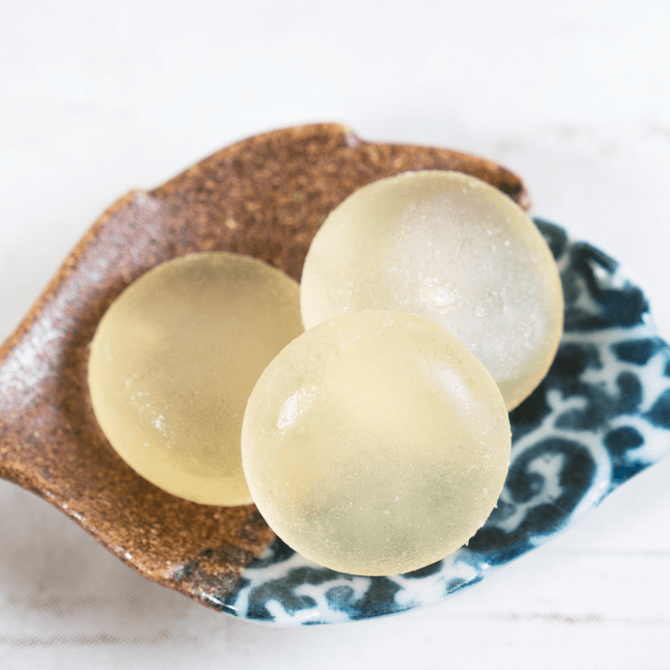 Close-up view of unwrapped KASUGAI Lychee gummies displayed outside the package, highlighting their smooth, chewy texture and lychee-inspired shape.