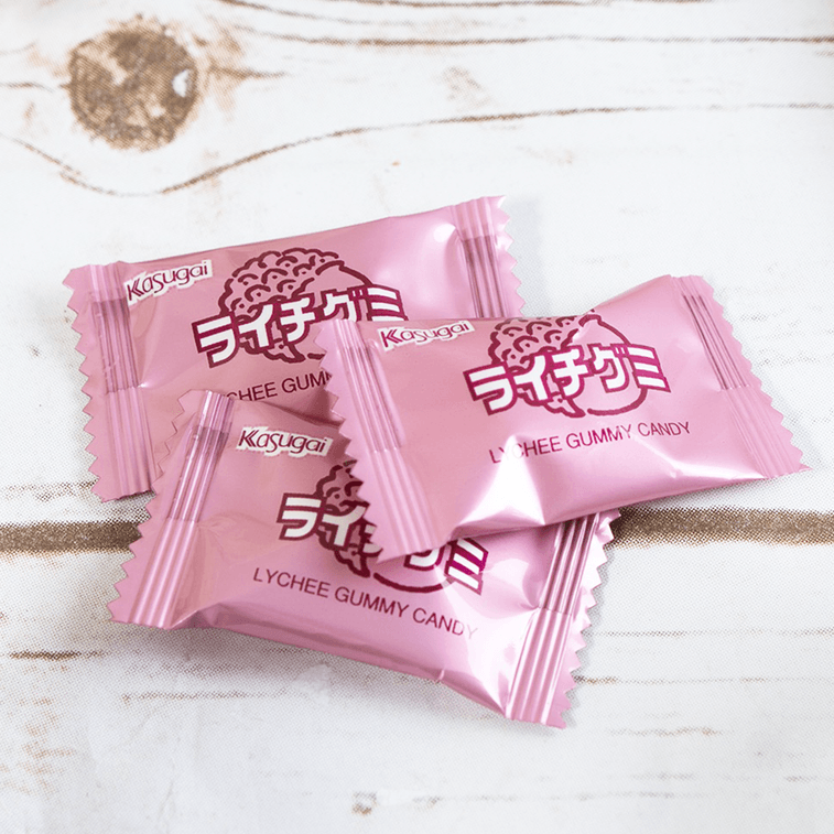 KASUGAI Lychee Gummy Candy served on a white plate, showing individual wrapped pieces and their soft, chewy texture outside the packaging.