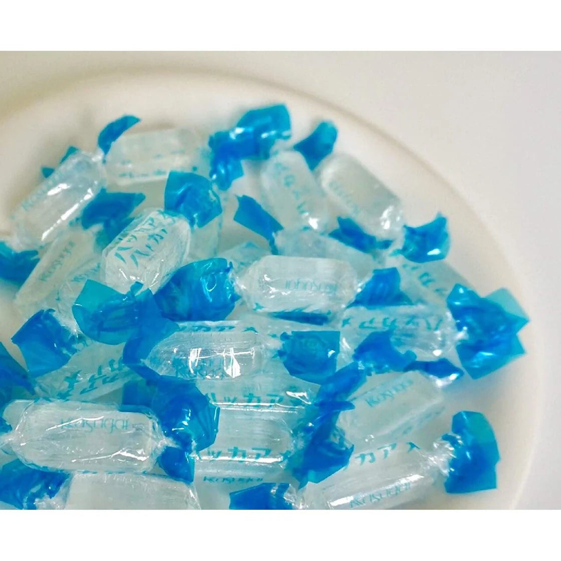 Several clear peppermint candies placed on a white plate alongside their wrappers, shown without the bag in the frame.