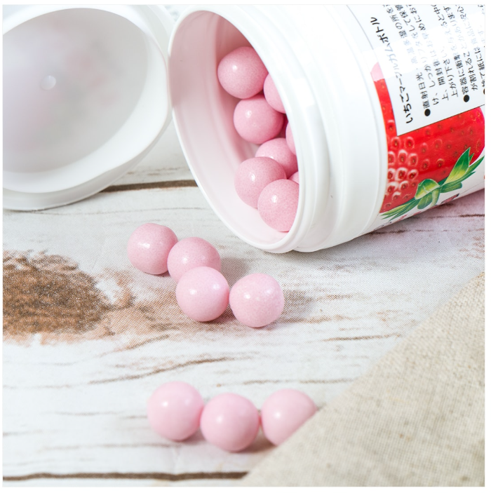 A portrait image showing the strawberry-flavored marble gums outside their bottle, with individually wrapped pieces arranged neatly on a white surface.